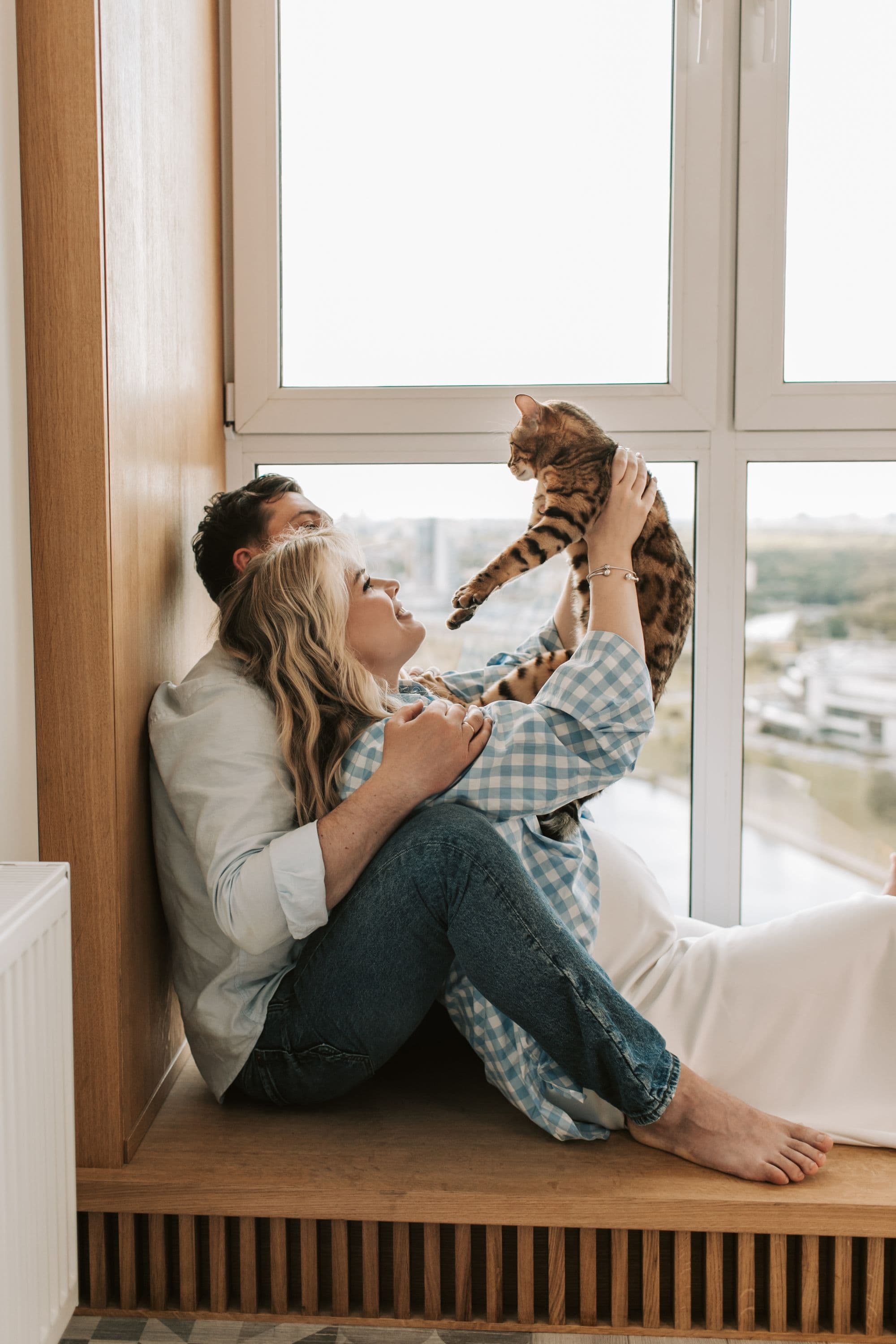 A couple playing with their cat by a sunny window