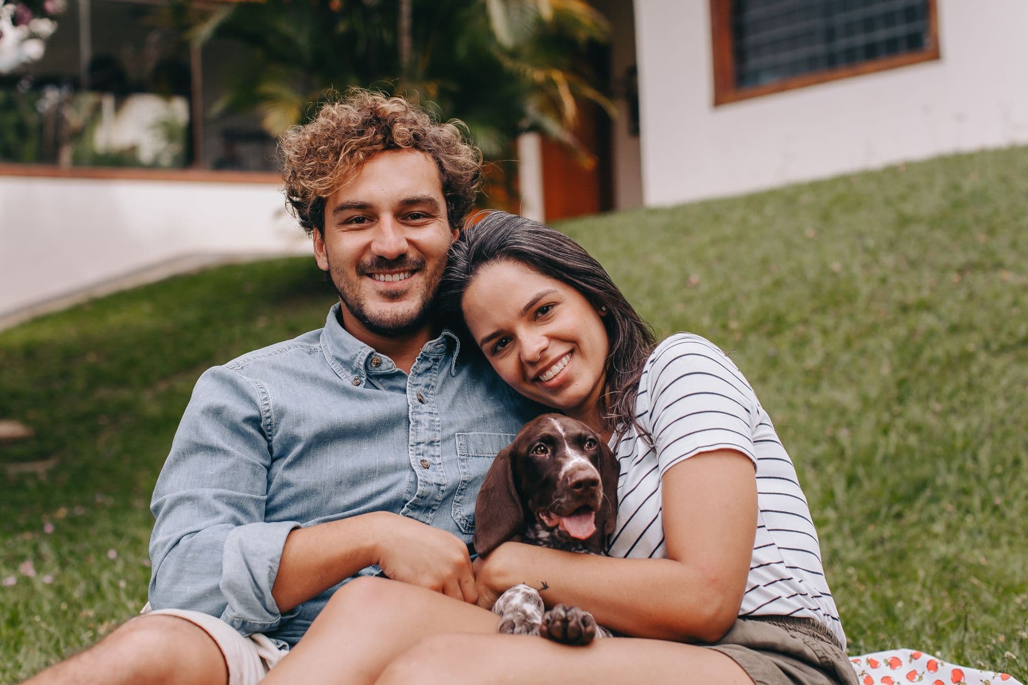 A couple sitting on the lawn with their spaniel puppy