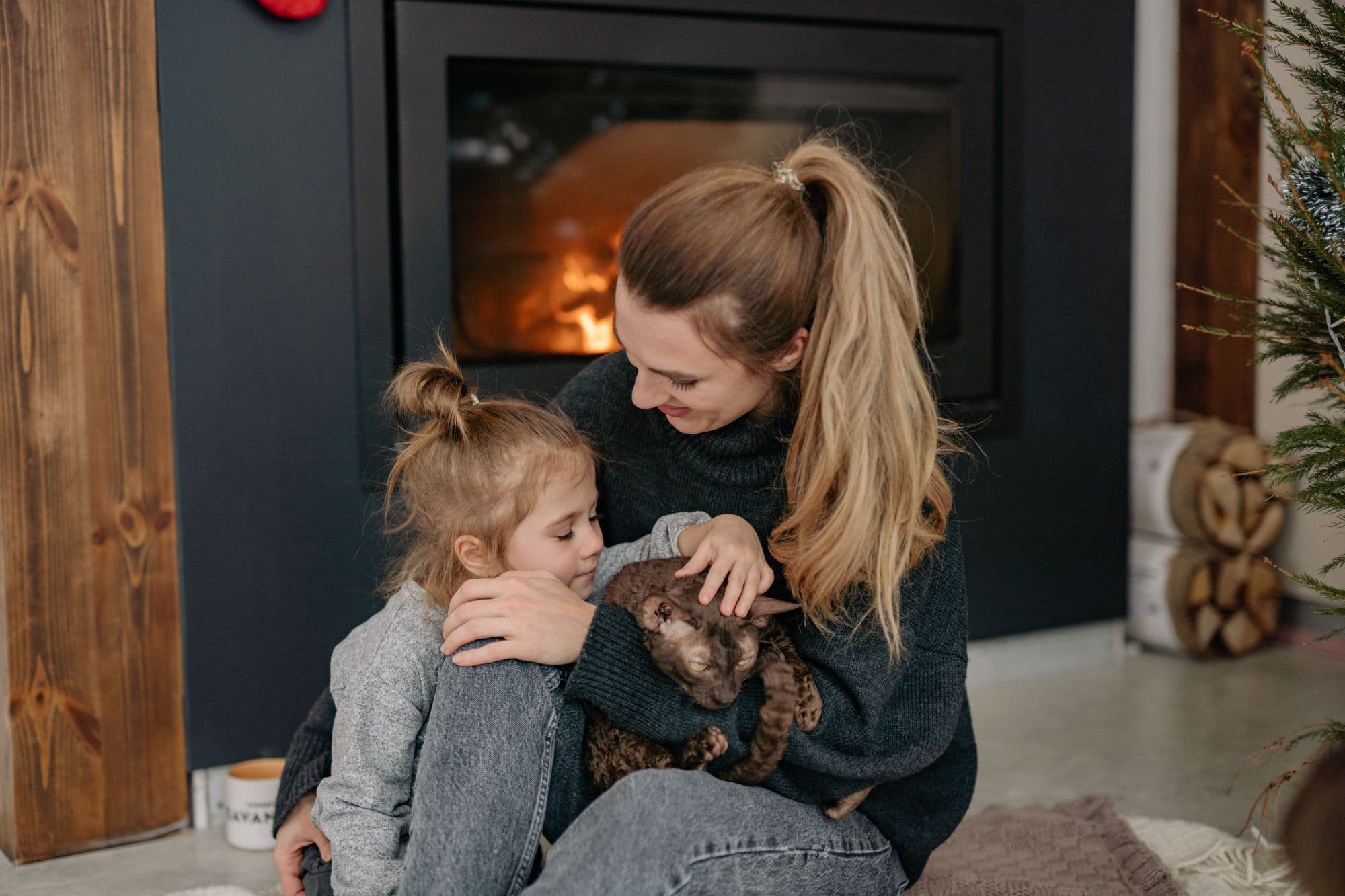 A mother and daughter cuddling their cat by the fireplace
