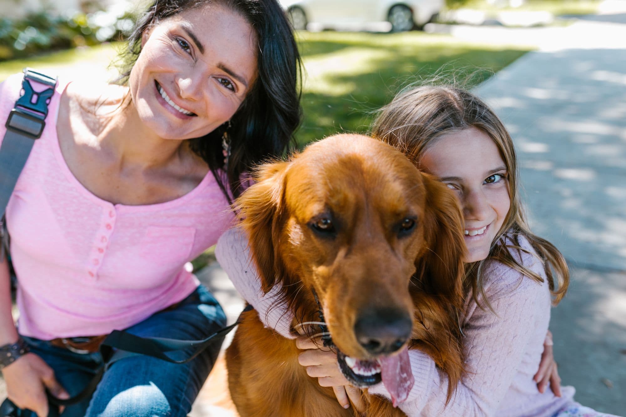A mother and daughter hugging their golden retriever